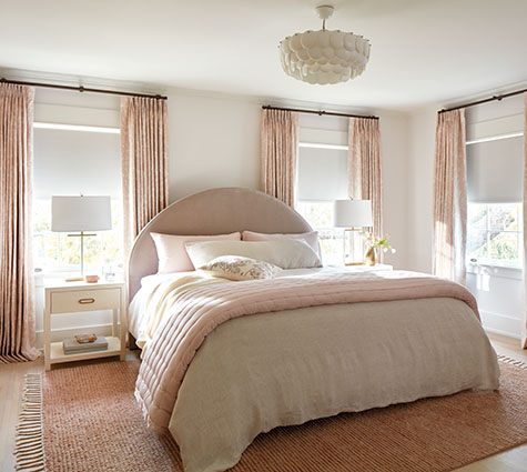 Layering styles, one of the in-style window treatment trends today, is seen in this bedroom's Tailored Pleat Drapery and Roller Shades