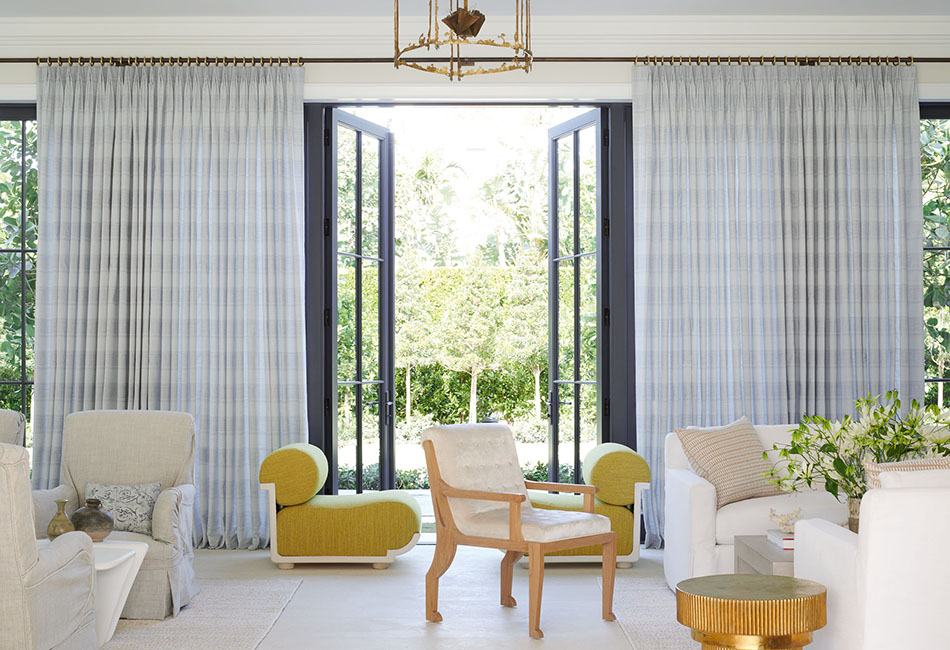 Curtains for living room spaces in soft sky blue add color and texture to a bright room with tall glass windows and doors.