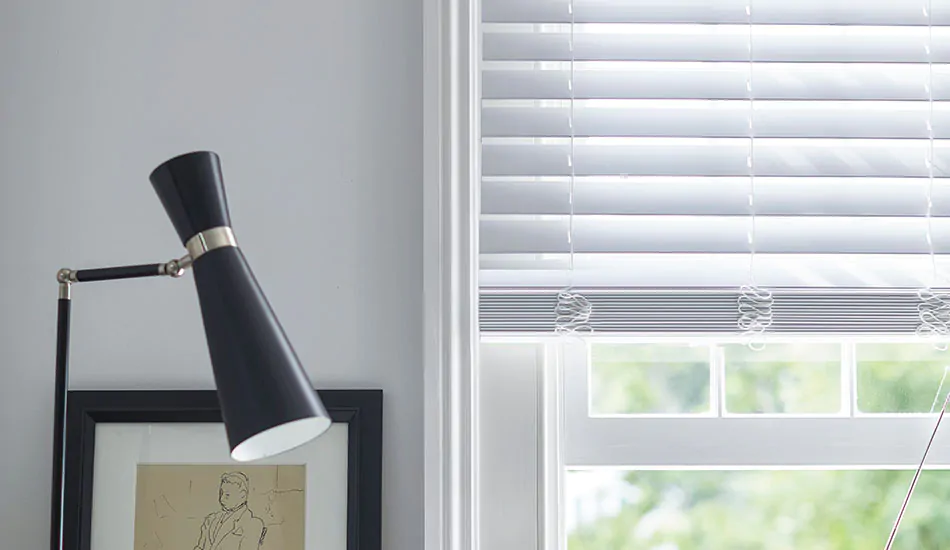 Faux Wood Blinds in Blanc hang partially down a window in a white room showing how to lower blinds halfway