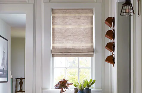 A Flat Roman Shade made of Shoreham Stripe in Oatmeal adds a warm, sandy color to a coastal hallway with a driftwood table