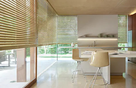 A bright, warm kitchen with tall windows has Metal Blinds made of Champagne giving the space an inviting golden hue as durable window treatments with adjustable privacy