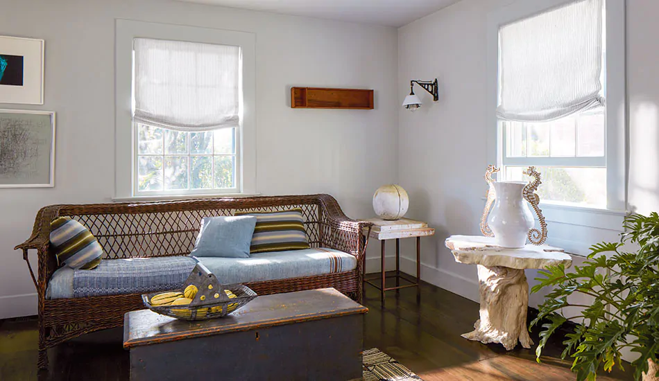 Contemporary window shade treatments in a coastal inspired sitting room include relaxed roman roman shades with subtle stripes