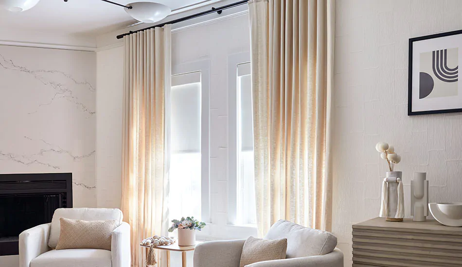 Modern window treatments in a bright family room include the stylish ripple fold drapery in a cream color over sleek roller shades