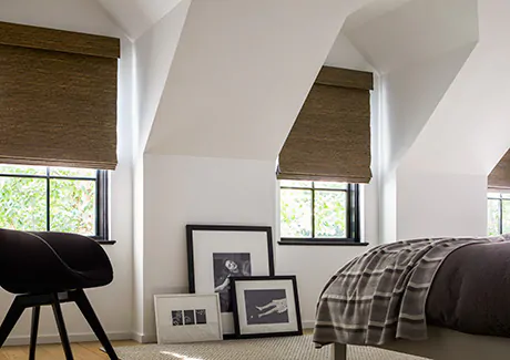 An attic bedroom features privacy shades in the Woven Wood Shade style made of Seaview material and featuring blackout lining as natural window coverings for full privacy