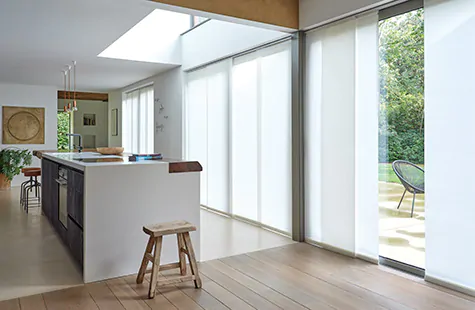 Vertical Blinds made of Park material in Winter run along a panel track in a large open kitchen with floor to ceiling windows as window coverings for large windows with privacy control