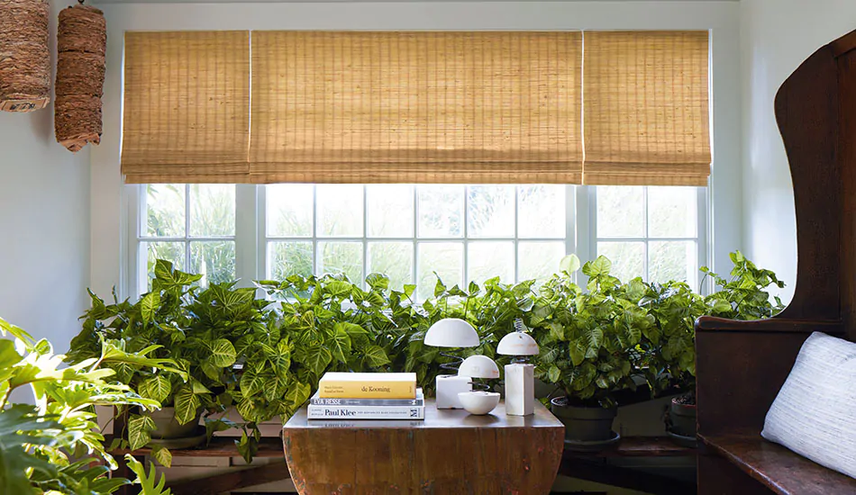 A bright sunroom features privacy shades in the Woven Wood Shade style made of Coastline material in Oat for a warm gold glow as interior window coverings with soft light and privacy